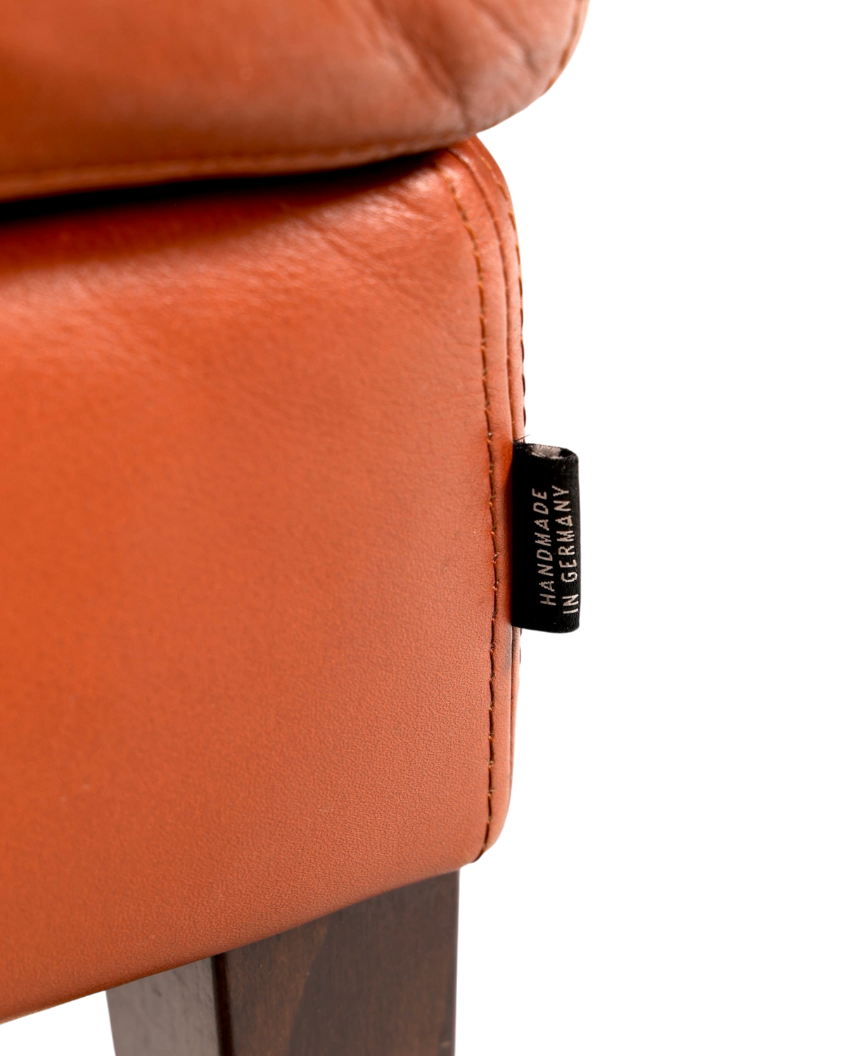 Hauptstadt Möblerei Hocker H896 aus cognacfarbenem Leder mit Handmade in Germany Etikett und dunklen Holzfüßen