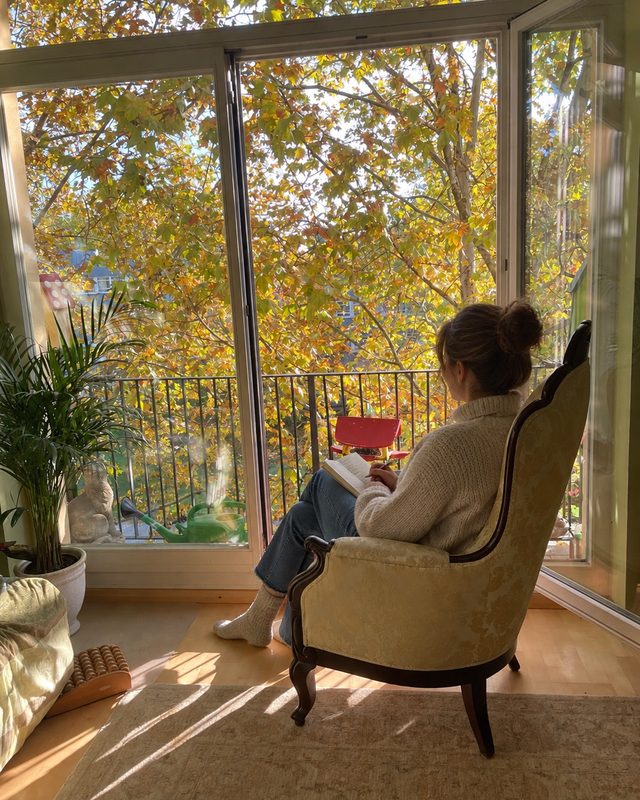 Cliente lisant dans un fauteuil près d’une fenêtre ouverte