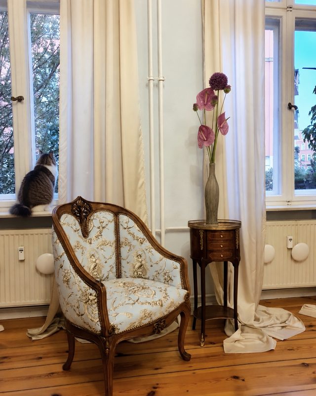 Fauteuil rembourré et petite table d’appoint devant une fenêtre d’un immeuble ancien